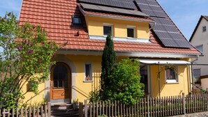 A yellow building with a red roof, solar panels, a wooden fence, and a small garden. - Cozy city apartment in Schwäbisch Hall (Schwäbisch Hall)