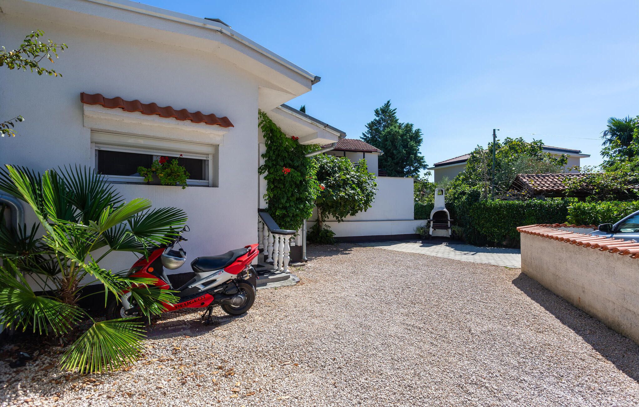 A residential area with a gravel driveway, a parked scooter, and a barbecue grill.