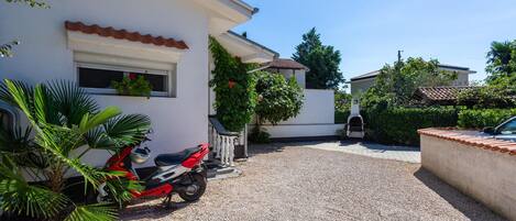 A residential area with a gravel driveway, a parked scooter, and a barbecue grill.