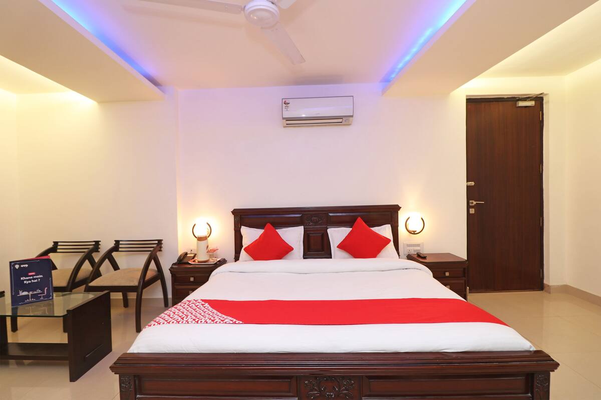 A hotel room with a bed, two bedside tables, a nightstand, a desk with chairs, and a door.