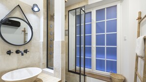 Une salle de bain dotée d’un grand lavabo ovale, d’un miroir, d’une douche avec une porte en verre et d’une fenêtre à vitrage dépoli.