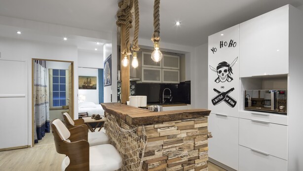 Une cuisine moderne avec un îlot central en bois, des tabourets de bar et un luminaire décoratif en forme de corde.