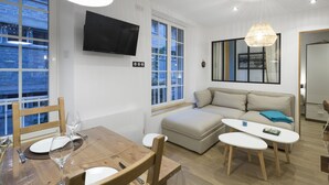 Un salon moderne avec une table à manger en bois, un canapé et un téléviseur fixé au mur.