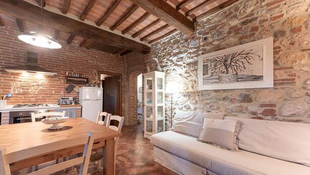 A cozy kitchen with a wooden table and chairs, a white sofa, and a stone wall with a framed picture. - Nice home in Civitella Marittima GR (Civitella Marittima GR)