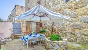 An outdoor dining area with a table set for four, a white umbrella, and stone walls. - Nice home in Civitella Marittima GR (Civitella Marittima GR)