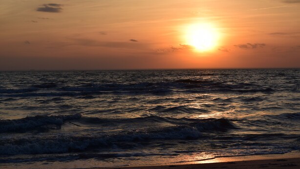 Un coucher de soleil sur l’océan, avec des vagues.