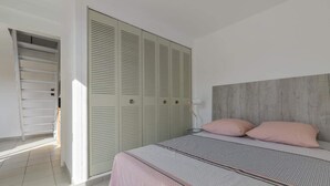 Ein Schlafzimmer mit einem Bett, zwei Kissen, einem Holzkopfstück und einem Schrank mit Klappläden.