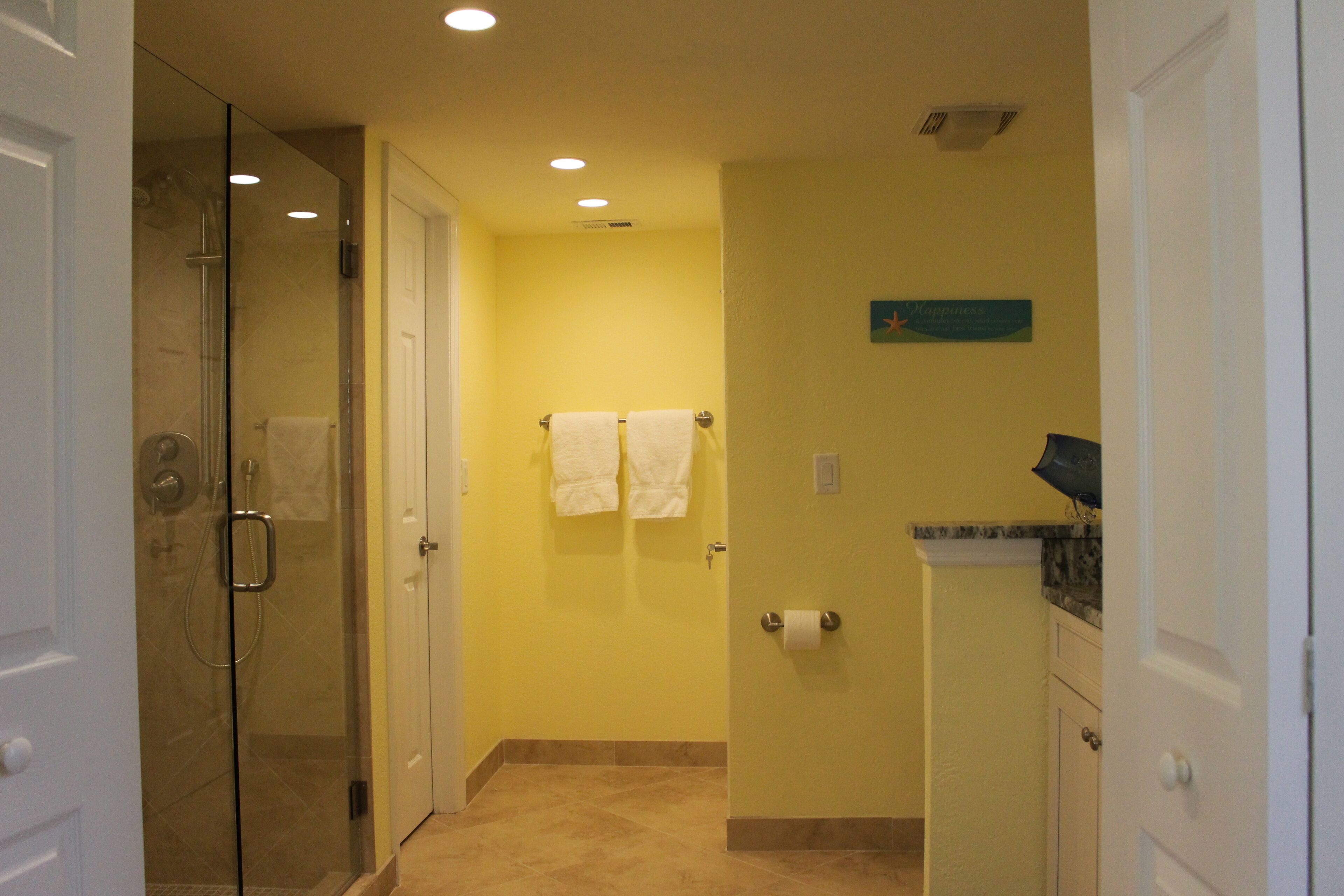 A bathroom with a glass shower enclosure, white towels, and a yellow wall.