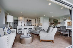 Relax in this inviting living area with a sofa, armchair, and coffee table, surrounded by a kitchen with white cabinetry and an island.