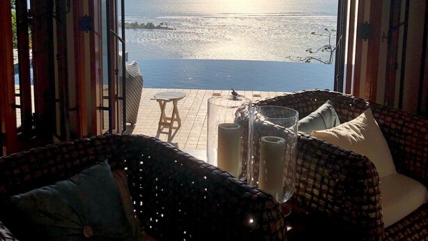 Una habitación con vistas al mar, un sofá de mimbre, una mesita y un vaso de agua.