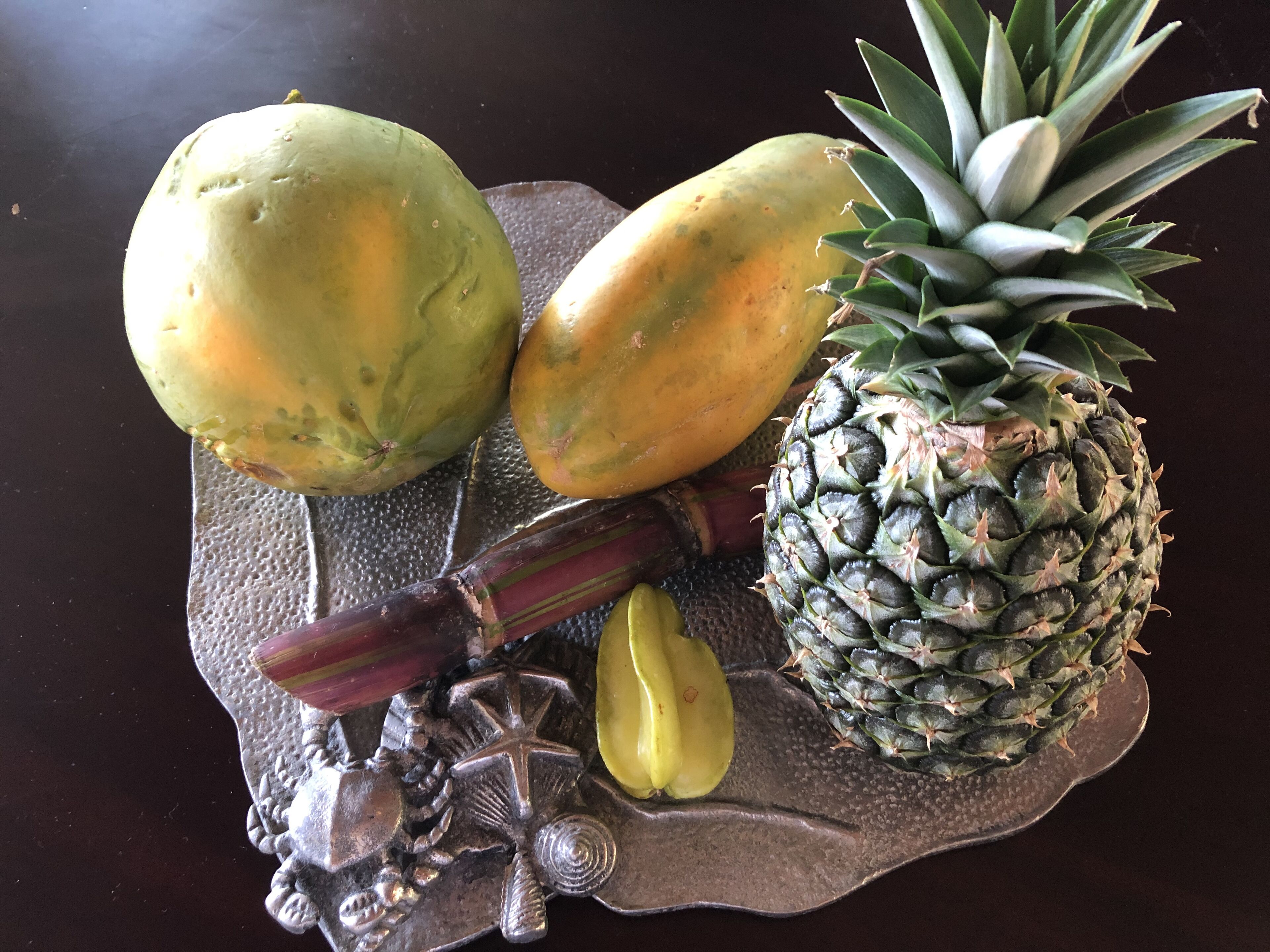Une assiette de fruits comprenant un ananas, des bananes et deux mangues, le tout disposé sur une assiette à texture particulière.
