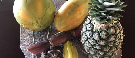 Une assiette de fruits comprenant un ananas, des bananes et deux mangues, le tout disposé sur une assiette à texture particulière.