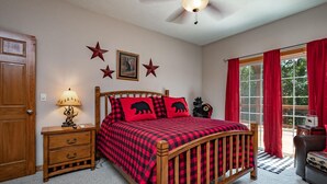 Ein Schlafzimmer mit einem hölzernen Bett, roten Vorhängen, einem Deckenventilator und einem Fenster mit roten Gardinen.