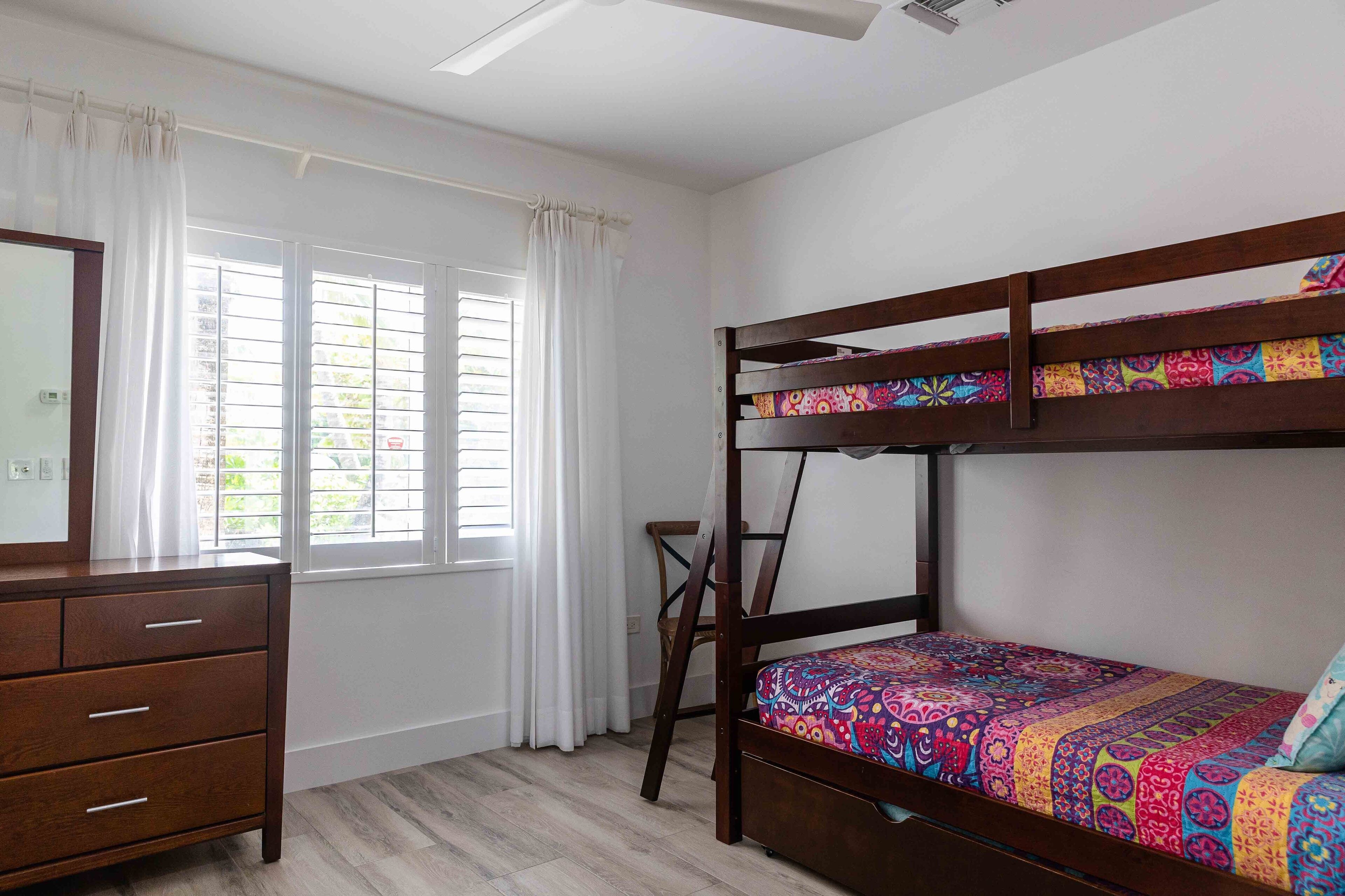 A bunk bed with colorful bedding, a wooden dresser, and a window with curtains.