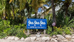 Une enseigne indiquant « SeaSeaSea », située au 1598, Rum Point Road, entourée d’une végétation tropicale et de palmiers.