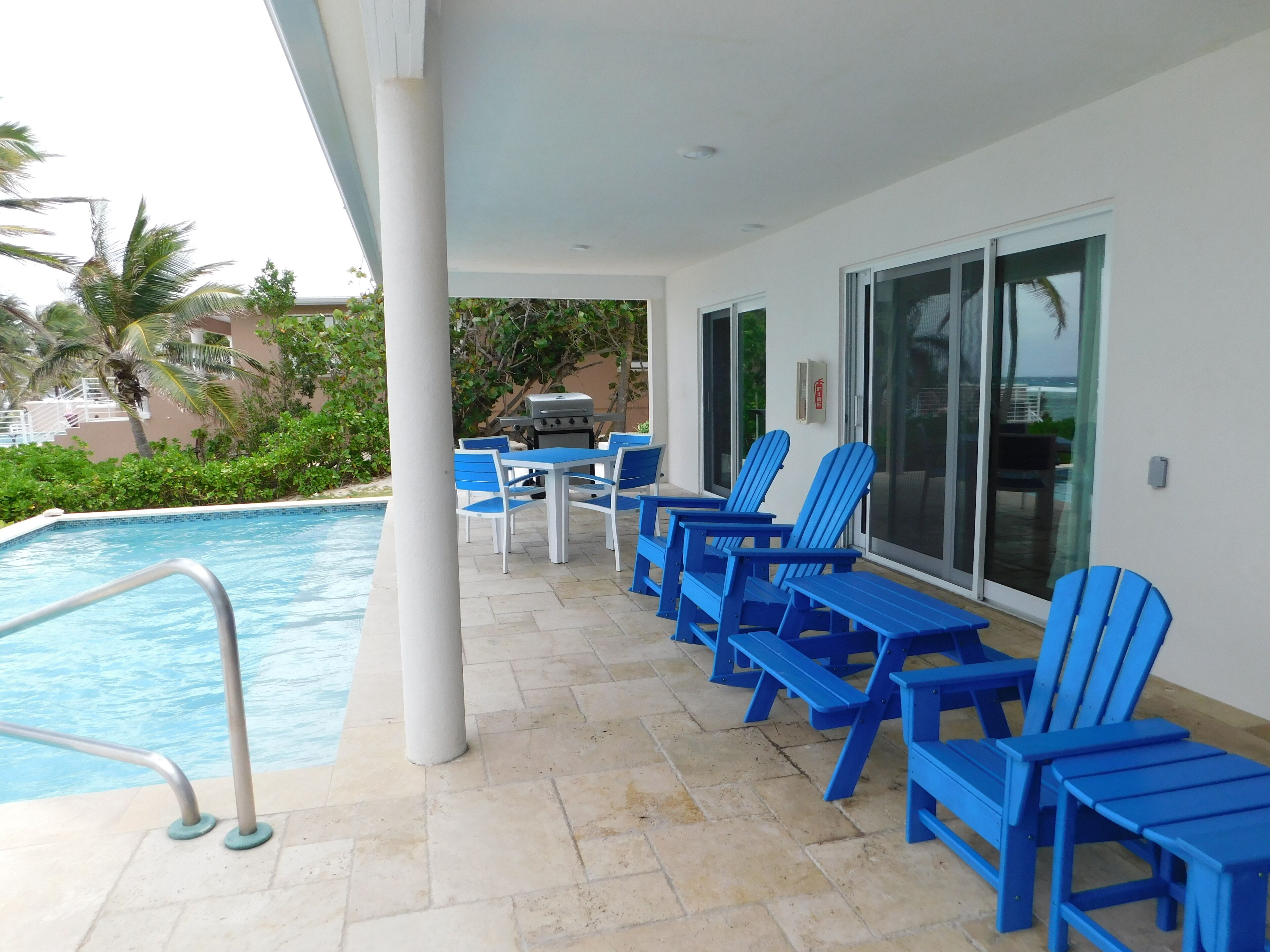 A poolside area with blue chairs, a table, and a grill.