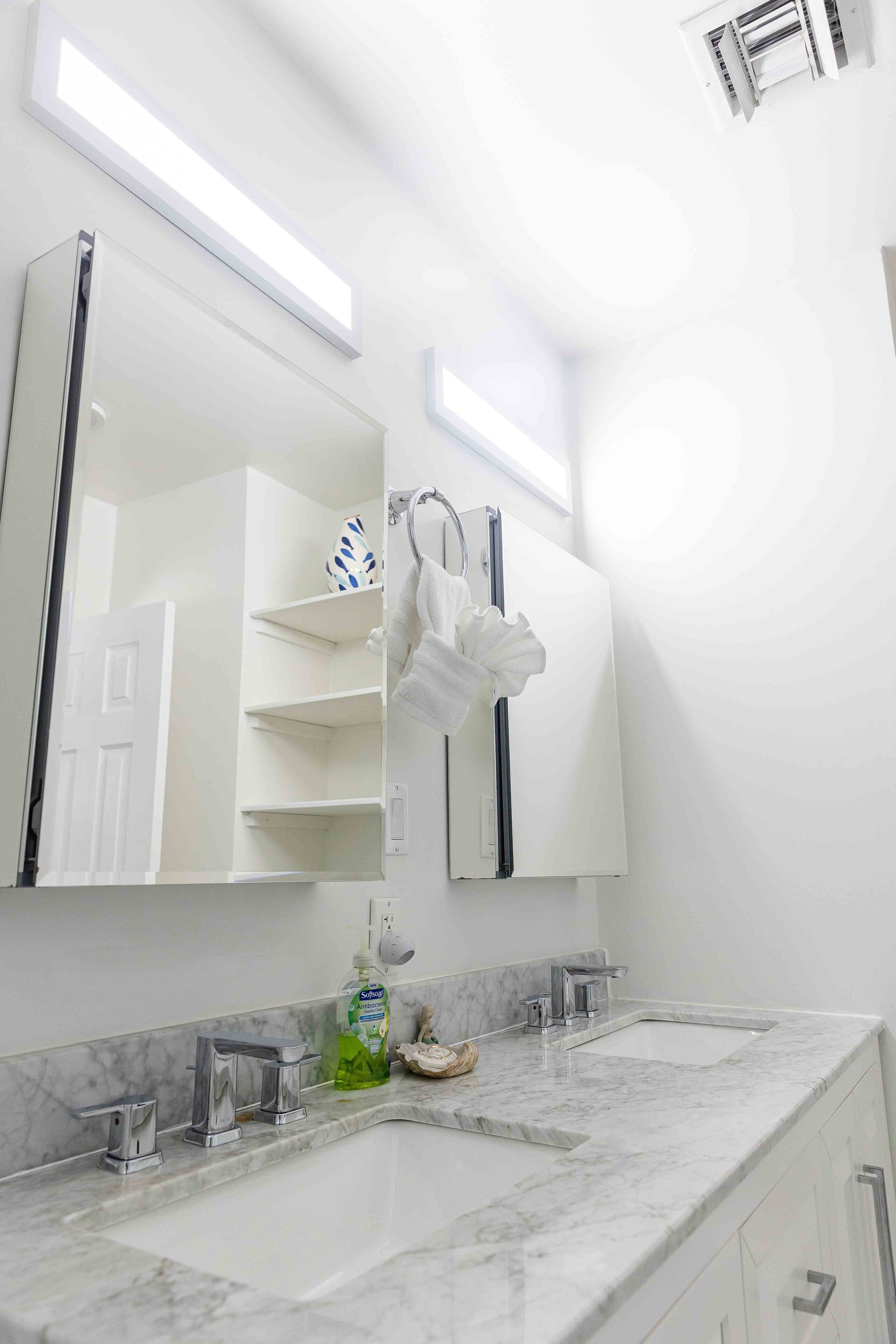 A bathroom with a large mirror, a towel rack, a shelf with toiletries, and a marble countertop.