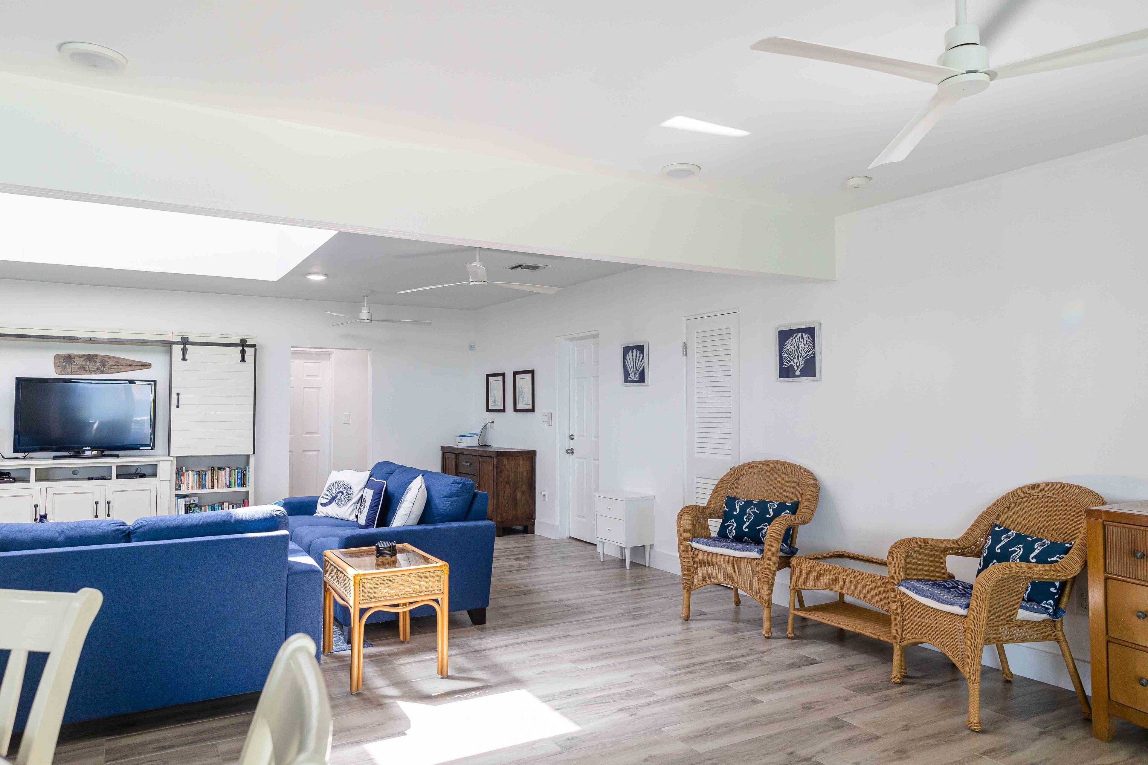 A spacious living room with a blue sofa, wicker chairs, a television, and a ceiling fan.