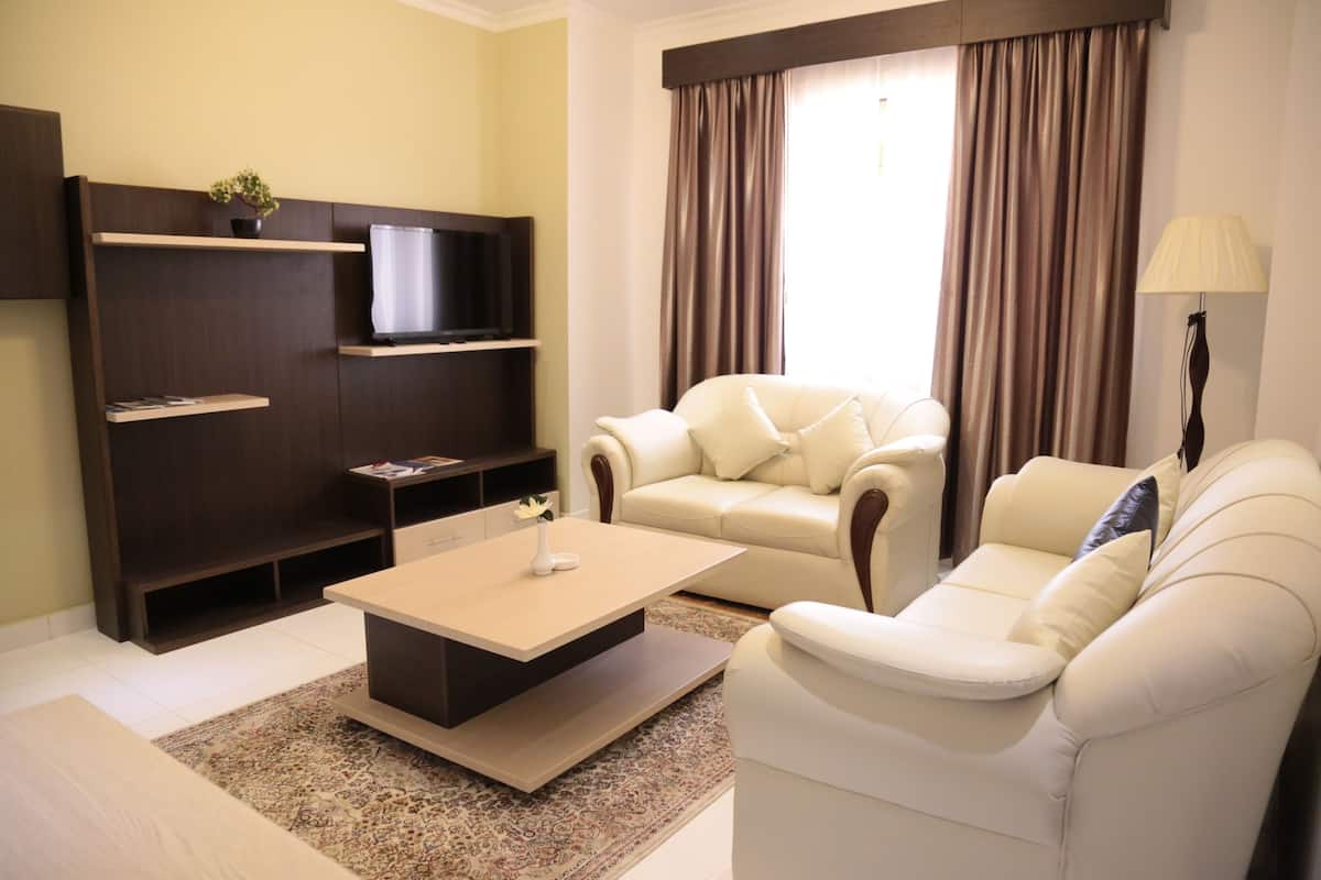 A modern living room with a beige sofa, a coffee table, a flat-screen TV on a dark wooden stand, and a large window with curtains.