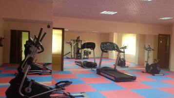 Uma academia com diversos equipamentos de exercício, incluindo esteiras e bicicletas ergométricas, em piso quadriculado.