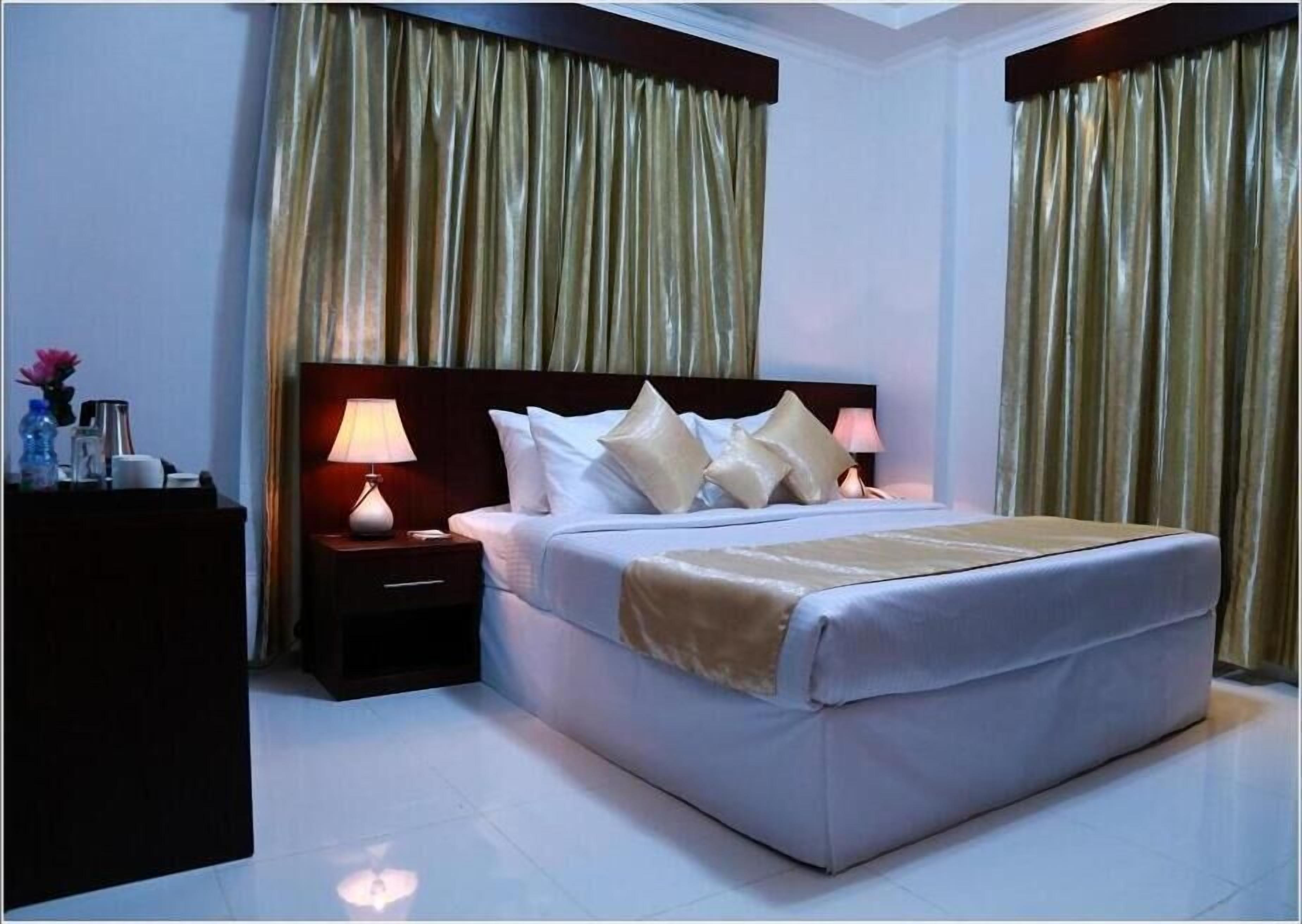 Une chambre d’hôtel avec un grand lit, deux tables de chevet avec des lampes et de lourds rideaux.