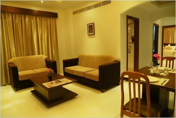 A living room with a sofa, armchairs, a coffee table, and a dining table with chairs. - Al Sadarah Hotel Apartments (Sohar)