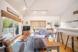 Un salon moderne comprenant un canapé, une table basse, un téléviseur et un coin repas avec des tabourets.