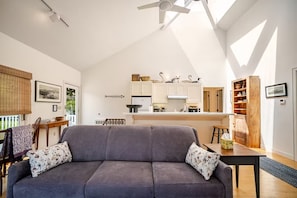 Een woonkamer met een grijze bank, een houten eettafel en een keuken met witte kasten.