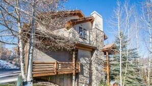A two-story house with a stone facade, wooden balcony, and a small front yard.