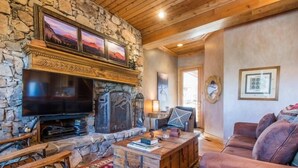 A cozy living room with a stone fireplace, a flat-screen TV, a leather sofa, and a wooden coffee table.