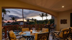 Un balcón con mesa lista para comer, con vista a una piscina y palmeras.