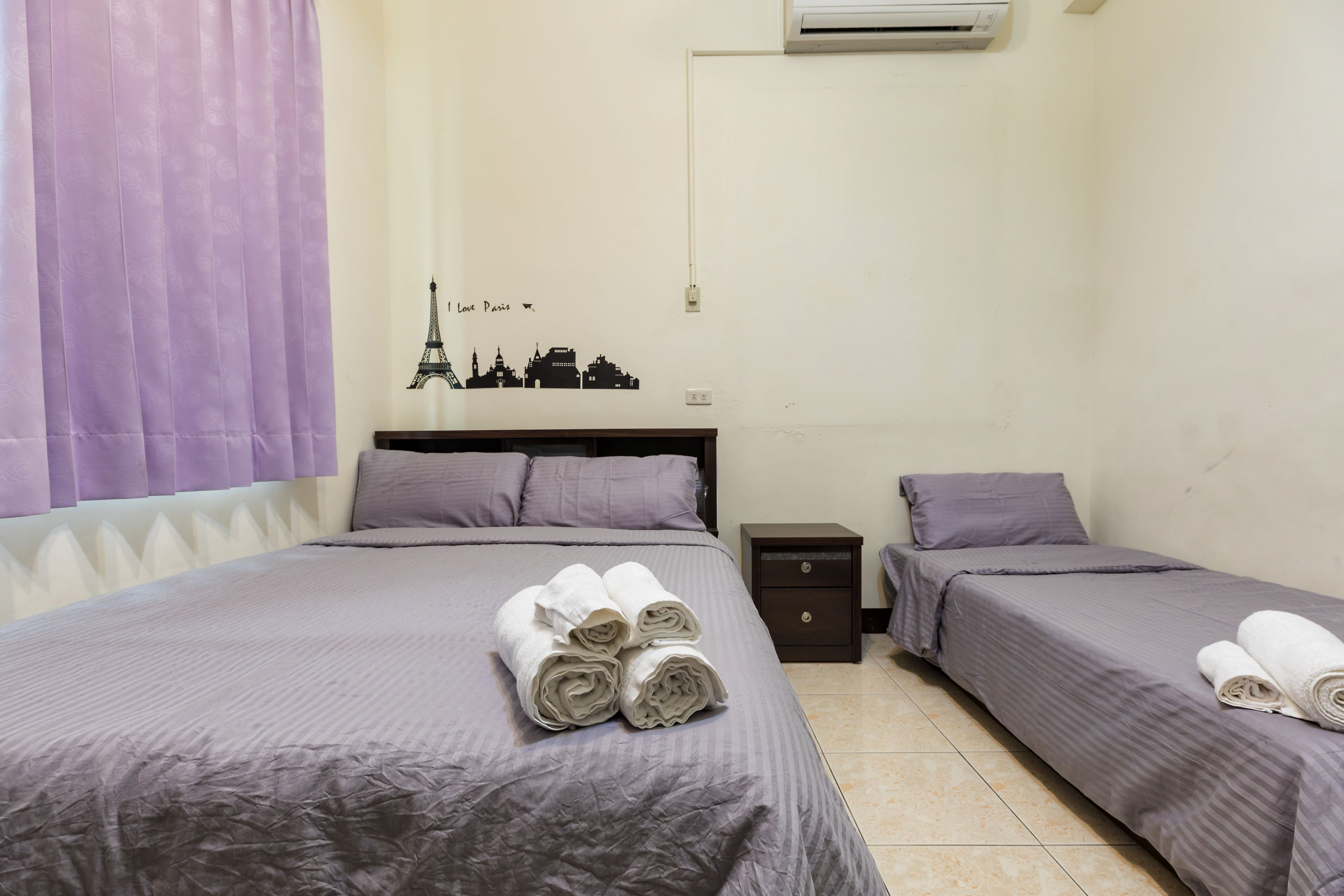 A hotel room with two beds, a nightstand, and a wall decal of Paris landmarks.