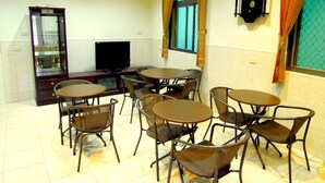 A dining area with round tables and chairs, a television, and a clock on the wall.