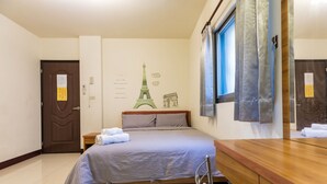 A hotel room with a bed, a wooden dresser, a window with curtains, and a wall with a Paris-themed mural.