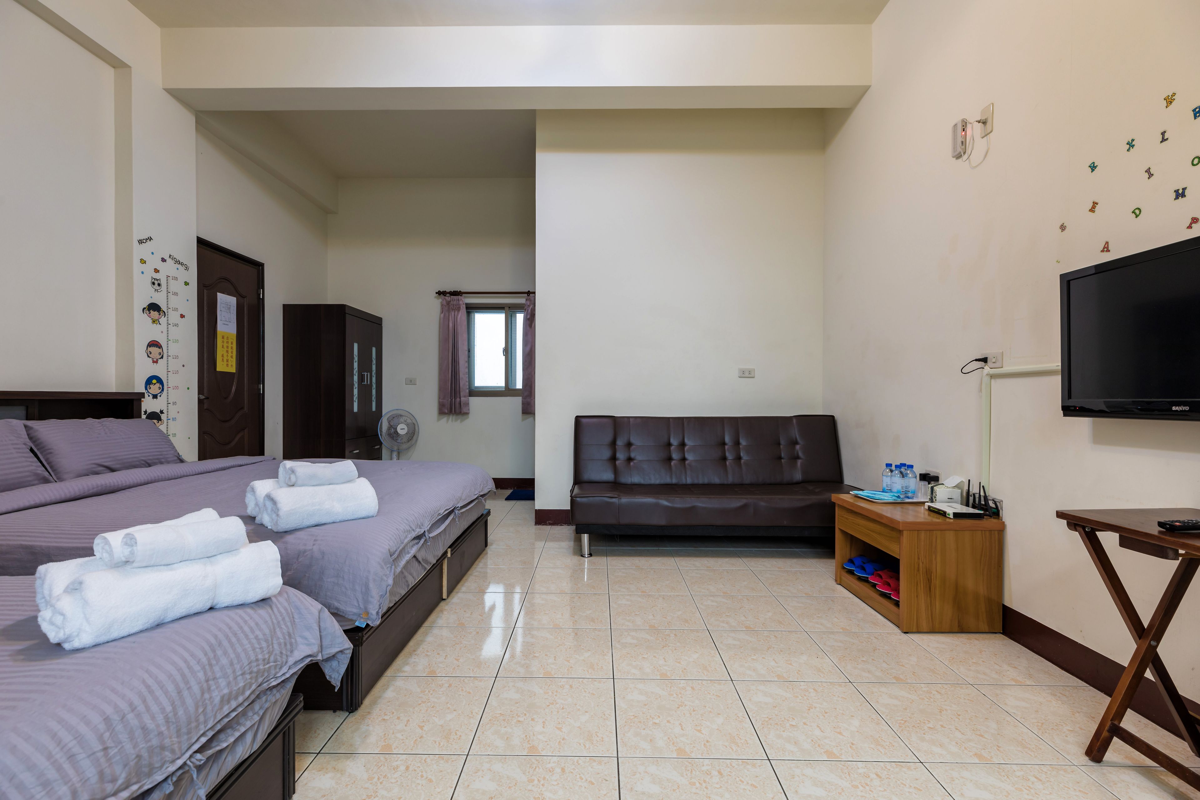 A hotel room with two beds, a sofa, a TV, and a small wooden side table.