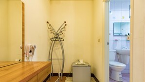 A bathroom with a wooden vanity, a hairdryer, a towel rack, a small cabinet, and a toilet.