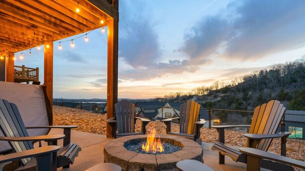 An outdoor seating area with Adirondack chairs, a stone fire pit, and string lights.