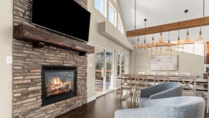 A modern living room with a stone fireplace, a flat-screen TV mounted above it, and a dining area with light wood furniture.