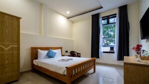A bedroom with a wooden bed, a wooden wardrobe, a TV on the wall, and a window with curtains. - Sum Villa Hoi An (Da Nang)