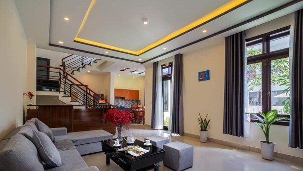 A modern living room with a sofa, coffee table, and a staircase leading to an upper floor. - Sum Villa Hoi An (Da Nang)