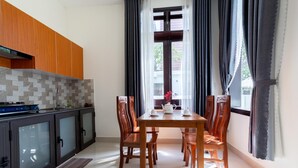 A modern kitchen with wooden cabinets, a tiled backsplash, and a dining area with a table and chairs. - Sum Villa Hoi An (Da Nang)