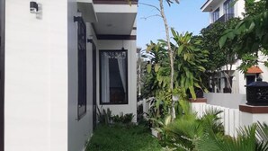 A modern building with a flat roof, a balcony, and a small garden area with grass and potted plants. - Sum Villa Hoi An (Da Nang)