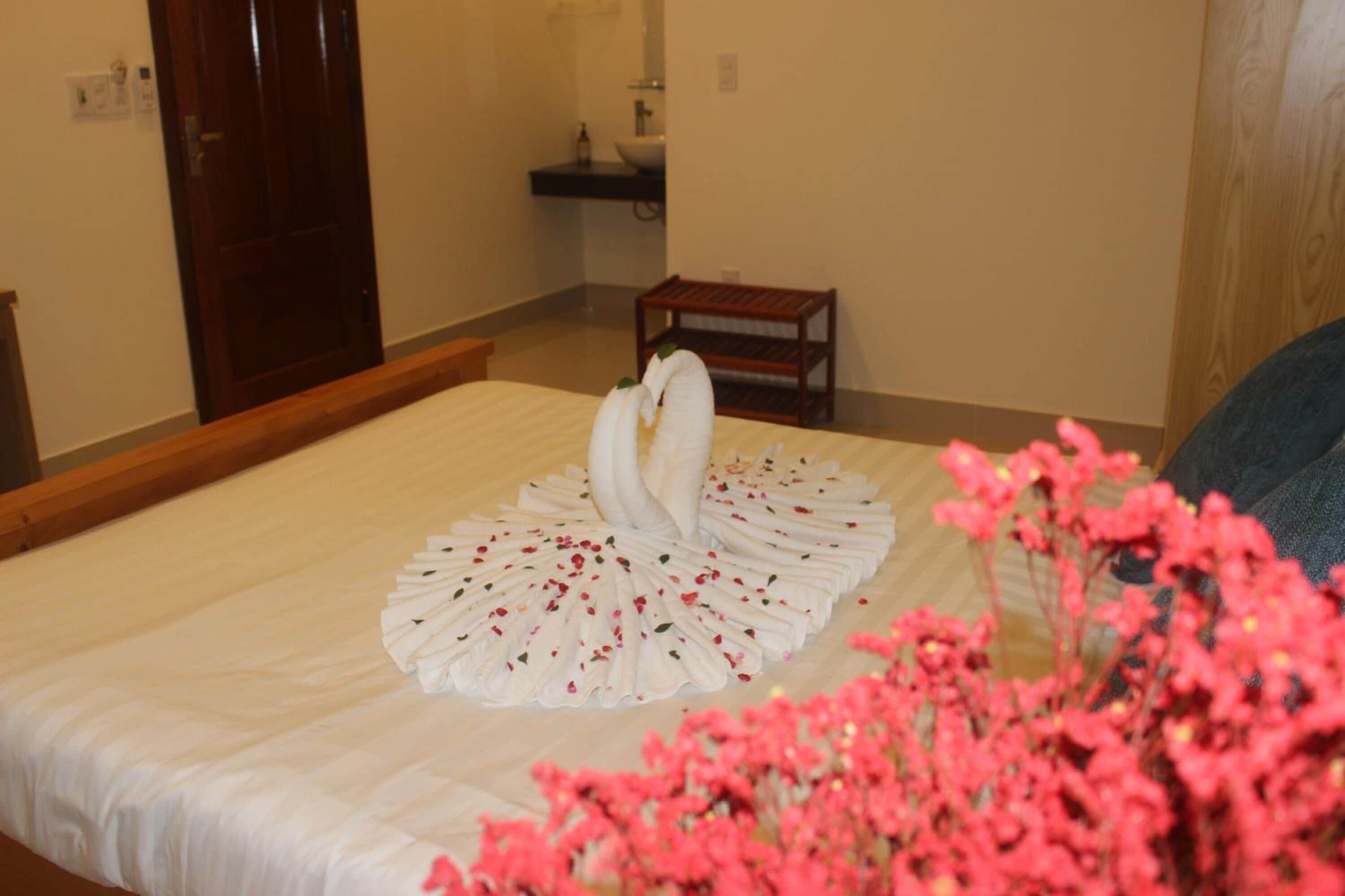 Una cama bien hecha con un arreglo decorativo de toallas y una pequeña mesita de madera.