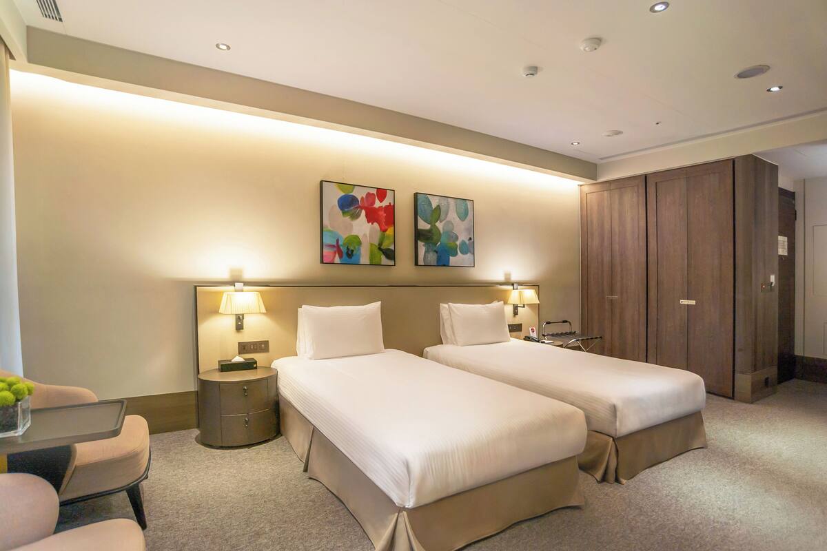 Une chambre d’hôtel avec deux lits, un bureau, une chaise, une armoire et deux lampes fixées au mur.