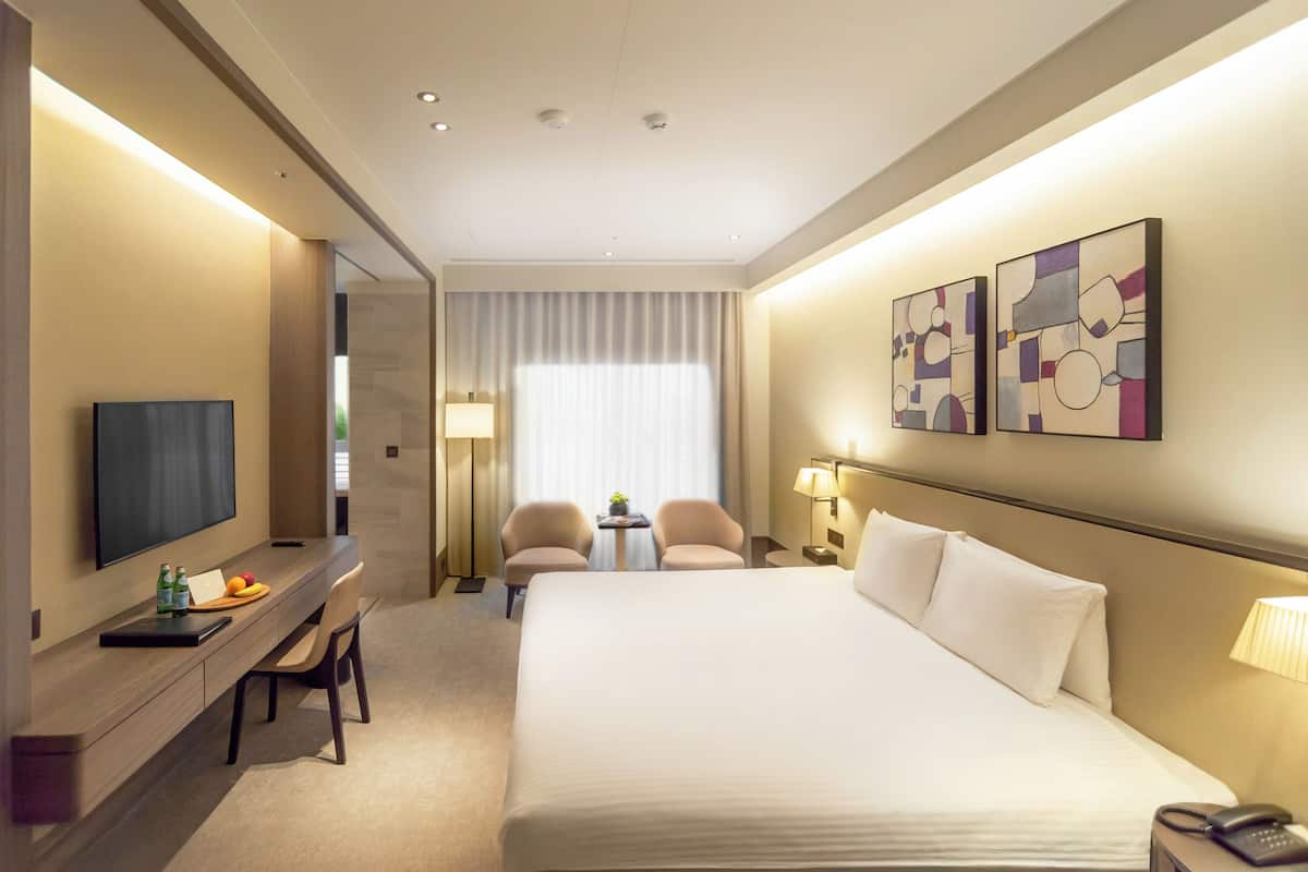 Une chambre d’hôtel dotée d’un grand lit, d’un bureau avec un téléviseur à écran plat, de deux chaises, d’une petite table avec une lampe et d’œuvres d’art accrochées au mur.