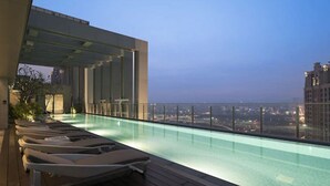 Una piscina en la azotea con sillones de descanso y vista a la ciudad.
