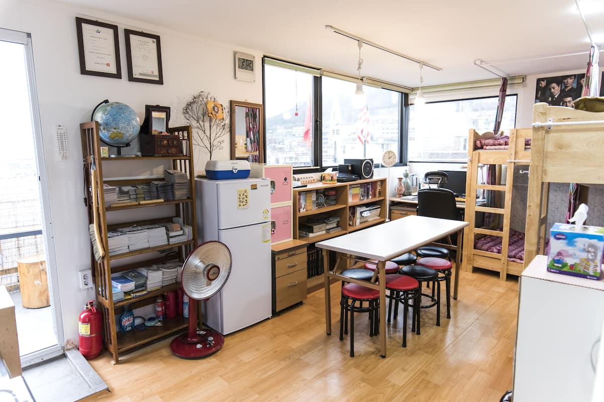 A compact room with a wooden table, chairs, a fan, and shelves with books and a globe.