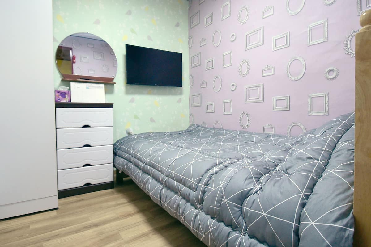 A bedroom with a bed, a dresser, a TV, and patterned wallpaper.