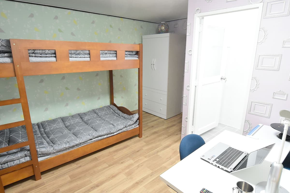 A bunk bed with a desk and laptop, a wardrobe, and a door with a decorative plate.