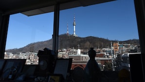 A view through a window of a cityscape with a prominent tower on a hill. - Photo Park Guesthouse (Seoul)